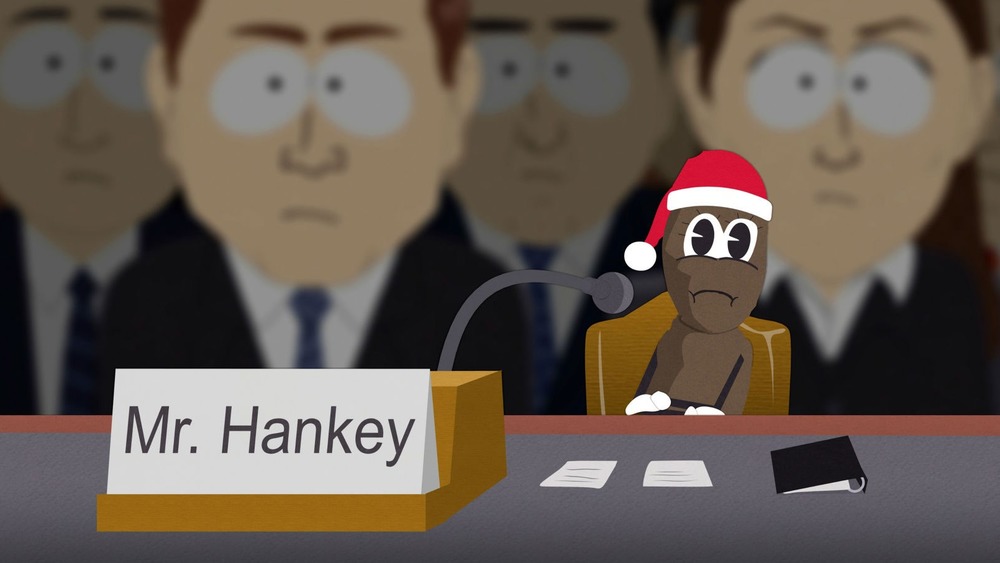 Mr. Hankey sits before a microphone and a nameplate on South Park