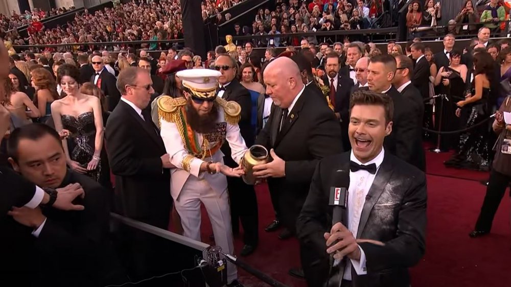 Sacha Baron Cohen as Admiral General Aladeen getting escorted away after dumping ashes on Ryan Seacrest