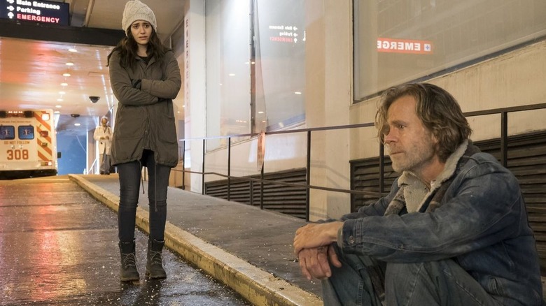 Emmy Rossum looks pitifully at William H. Macy sitting on a curb