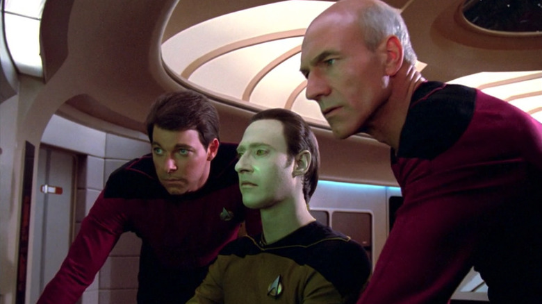 Riker, Data, and Picard look at a monitor