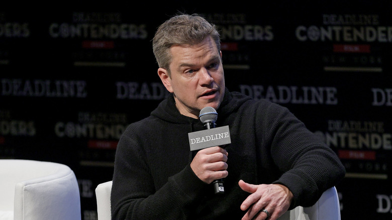 Matt Damon responding to a question sitting in a chair with a microphone in hand