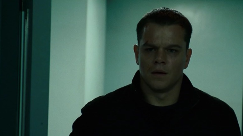 Jason Bourne standing in front of a white wall looking tired