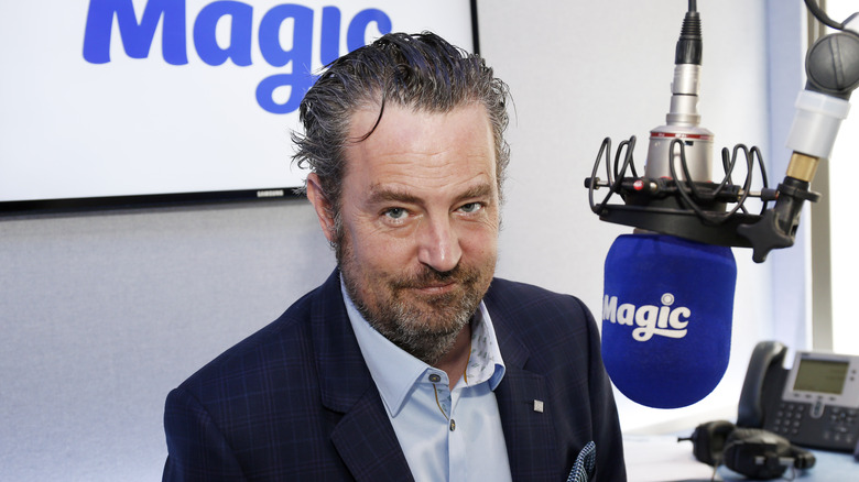 Matthew Perry smiles in front of a microphone