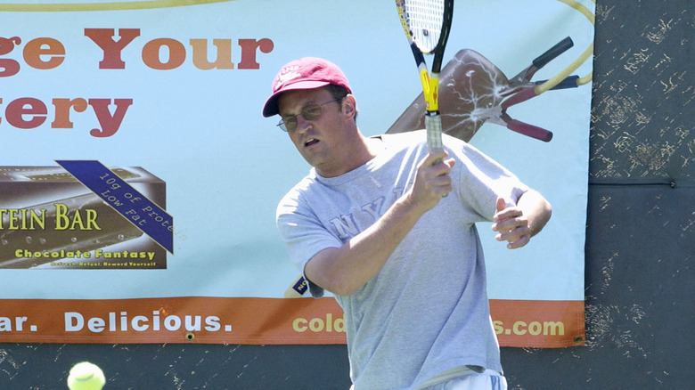 Matthew Perry swings a tennis racket