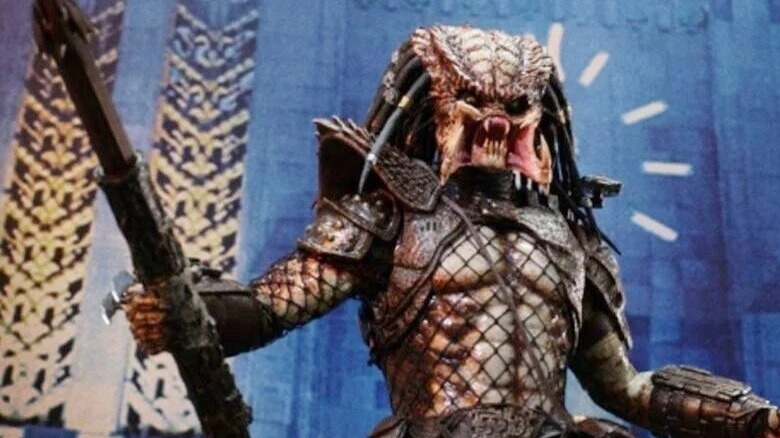 The unmasked Predator holding a spear