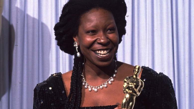 Whoopi Goldberg smiling and holding Oscar