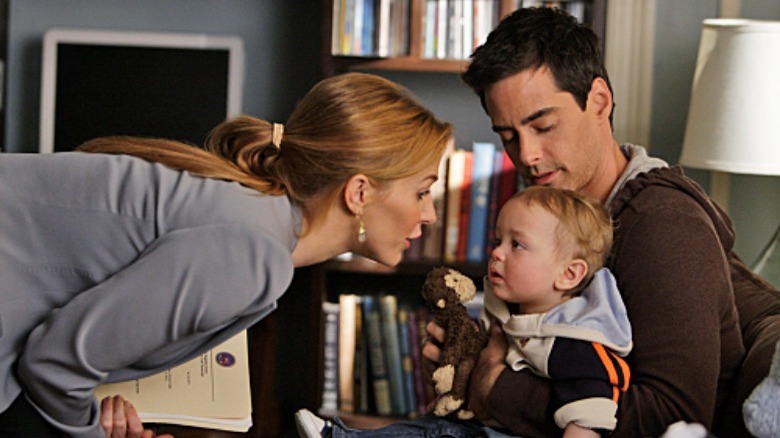 Adam Kaufman holding a baby as Poppy Montgomery leans in