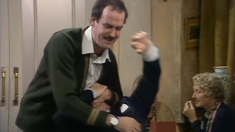 Basil Fawlty manhandling a visitor