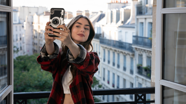 Lily Collins as Emily Cooper holding camera phone in Emily in Paris