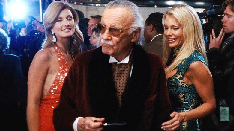 Stan Lee flanked by two beautiful women