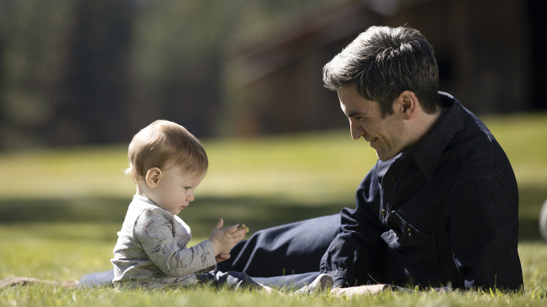 Jamie sits with his baby in the grass