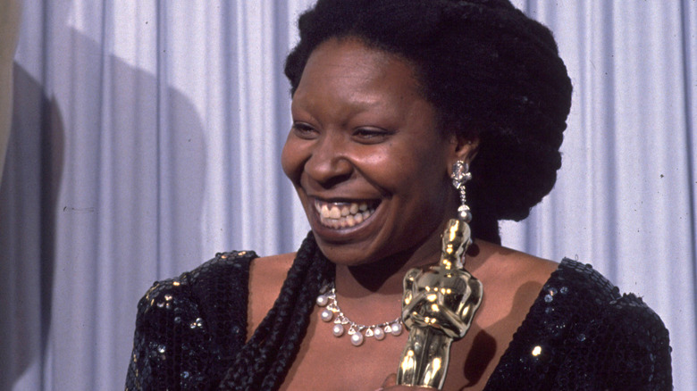 Whoopi Goldberg smiles broadly while holding Oscar