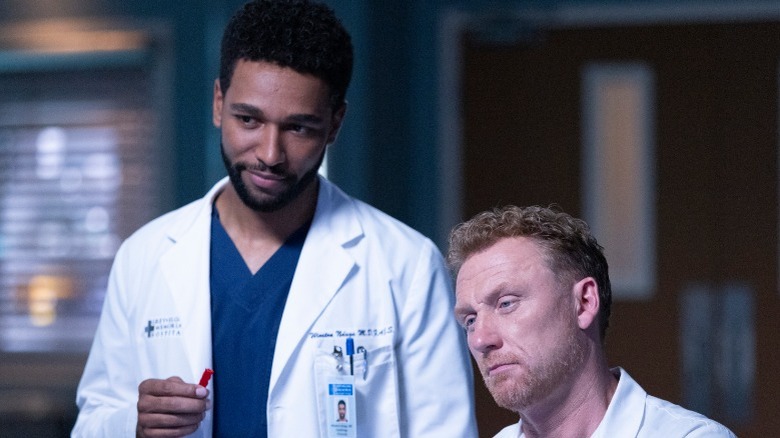 Dr. Winston Ndugu stands and smiles while Dr. Owen Hunt sits next to him