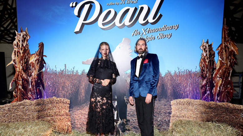 Mia Goth and Ti West in front of a large poster for Pearl