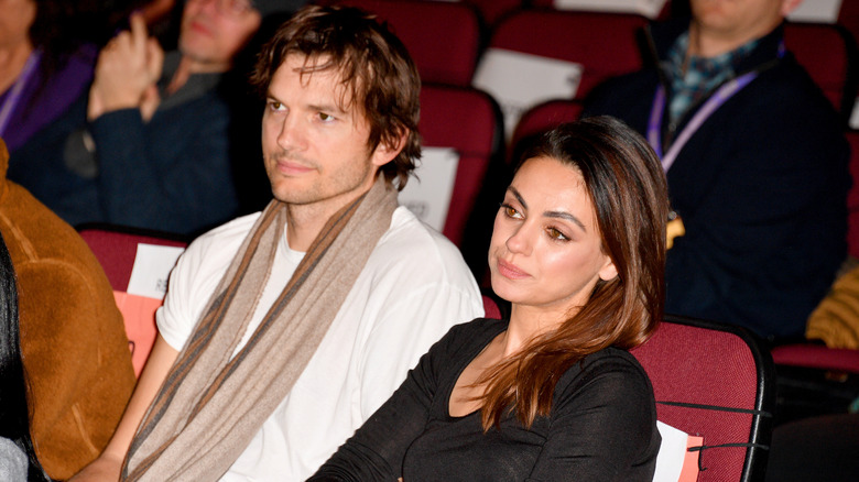 Mila Kunis sitting with Ashton Kutcher