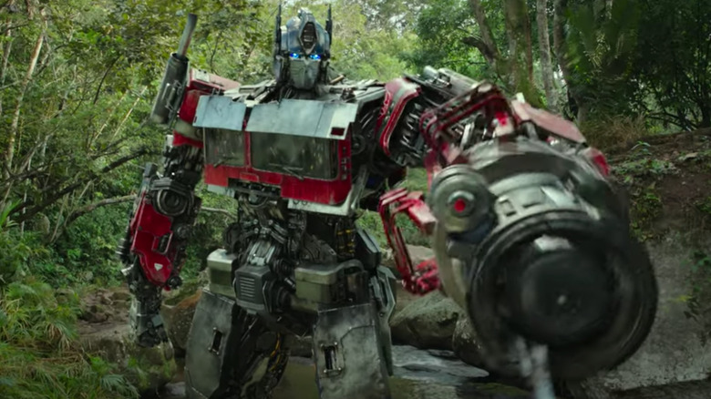 Optimus Prime standing in forest with his arm weaponizing