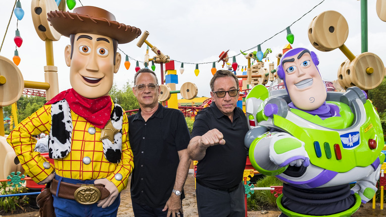 Tom Hanks and Tim Allen standing with Woody and Buzz Lightyear