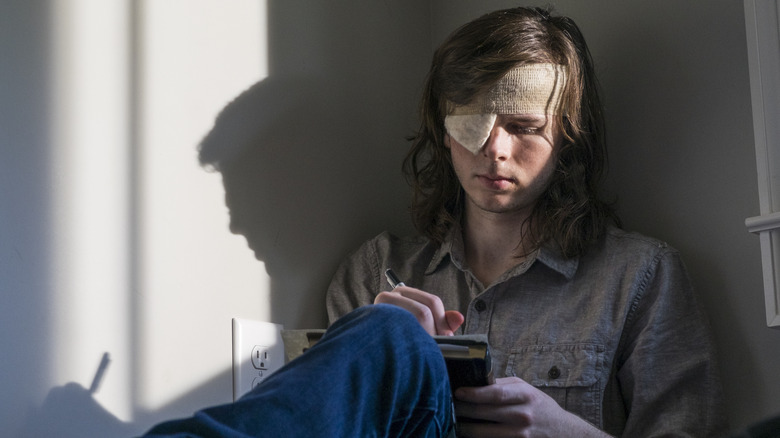 Carl with a bandage over his eye sitting and writing in a notebook