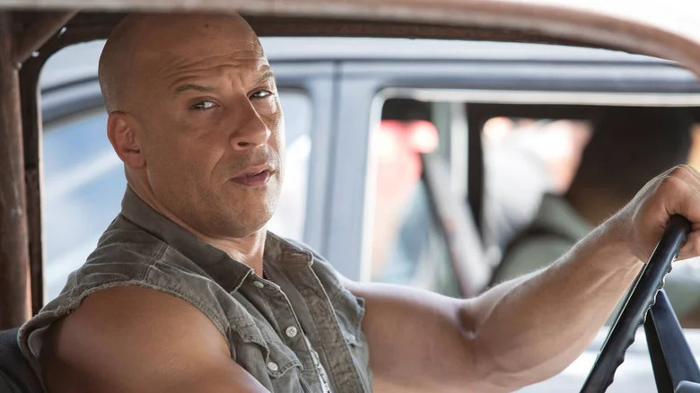 Bald Dom Toretto driving car in denim vest