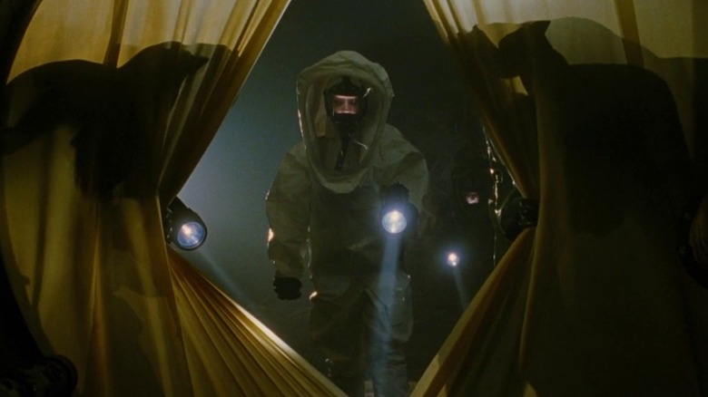 Figure in Hazmat suit holds flashlight