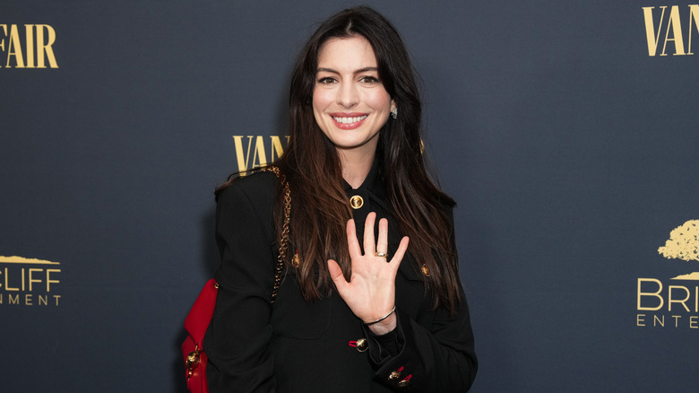 Anne Hathaway waving to the camera at a red carpet event in 2024.