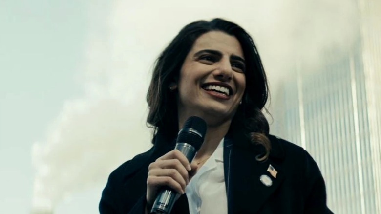 Neuman speaking into a microphone in her right hand while smiling before a smoke-obscured skyscraper