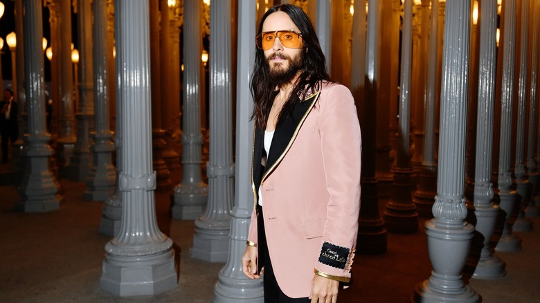 Jered Leto stands dressed in tinted sunglasses and a pink blazer