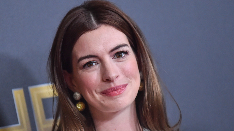 Anne Hathaway smiles in front of dark blue backdrop