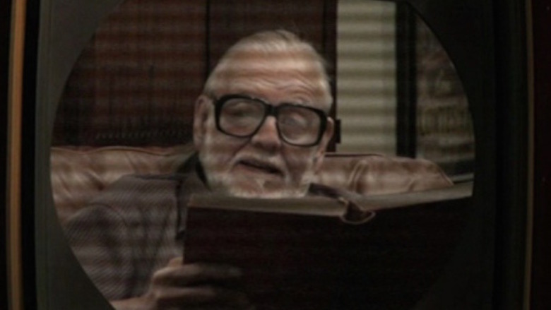 George Romero seen on a TV screen reading a book