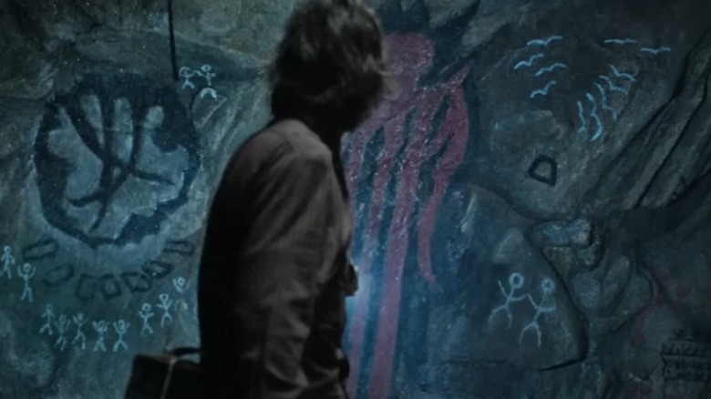 Victor stands in front of cave art of an entity that looks like a red jellyfish