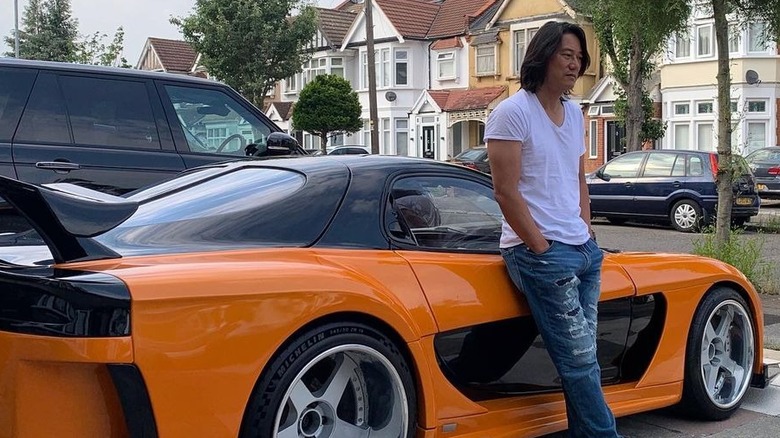 Sung Kang leaning against an orange Mazda RX-7 FD