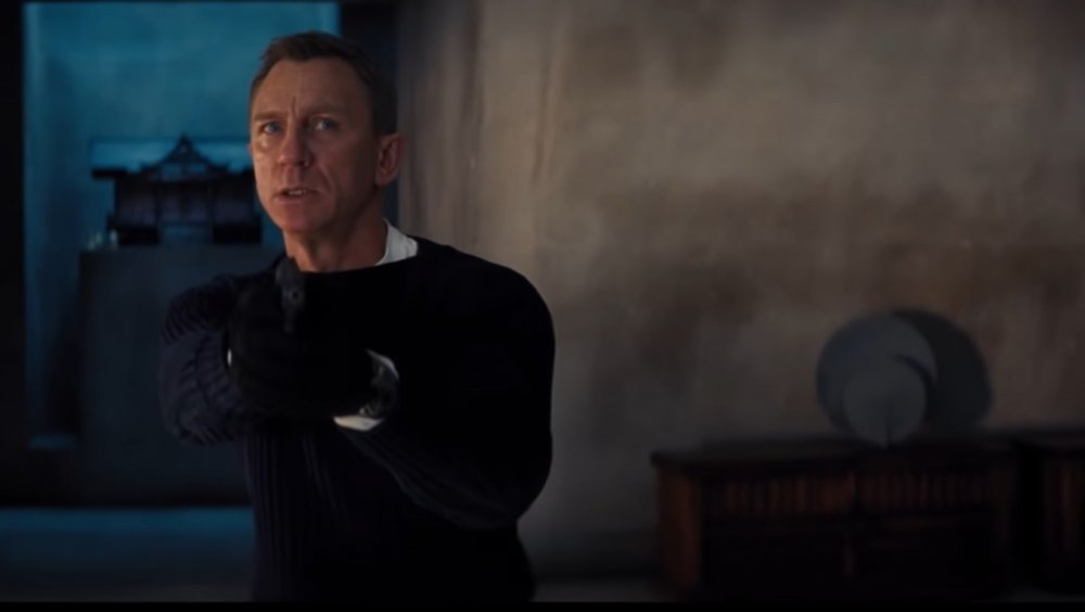 Daniel Craig as James Bond pulls his gun in No Time to Die