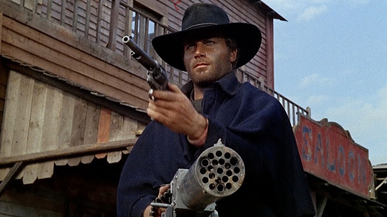 Django holding a revolver and a machine gun in a Western town