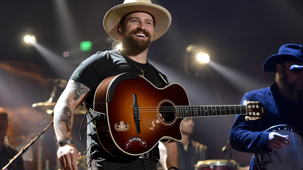 Zac Brown smiling, wearing a guitar on stage 