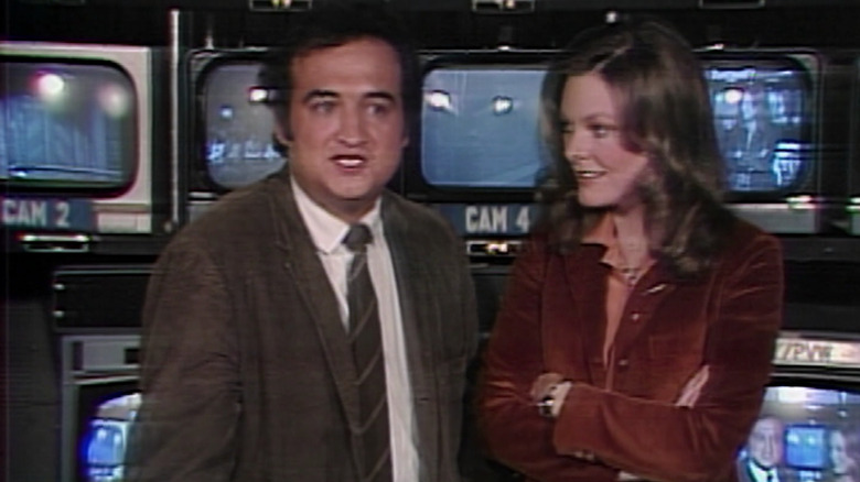 Belushi and Curtin talking by screens