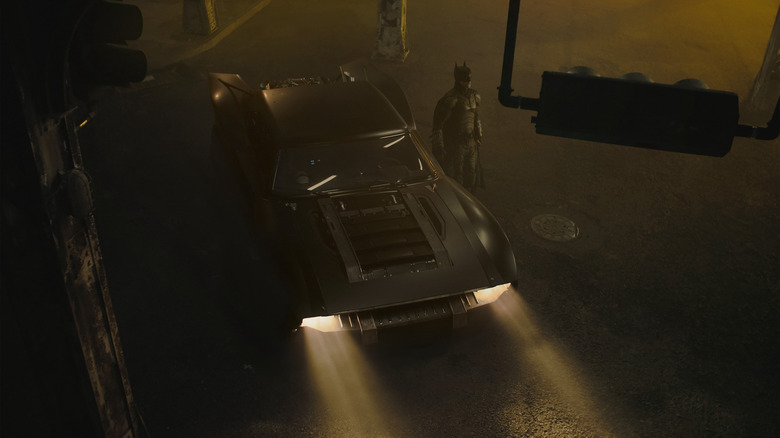 Batman next to Batmobile in Gotham City at night