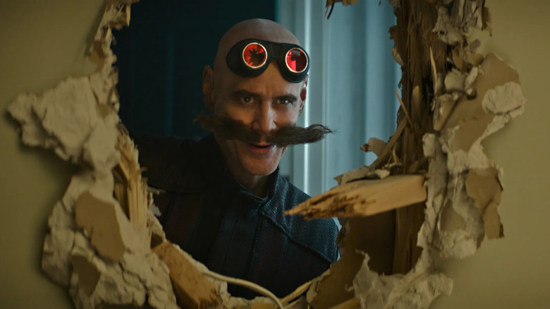 Jim Carrey as Ivo Robotnik looks through a hole in a wall.