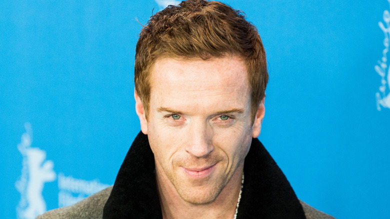 Damien Lewis smiles while wearing an overcoat