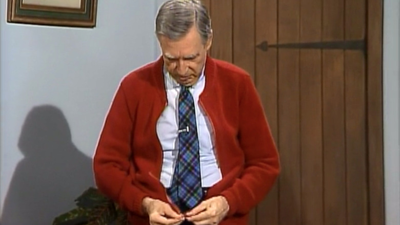 Mister Rogers attempts to zip up his cardigan.