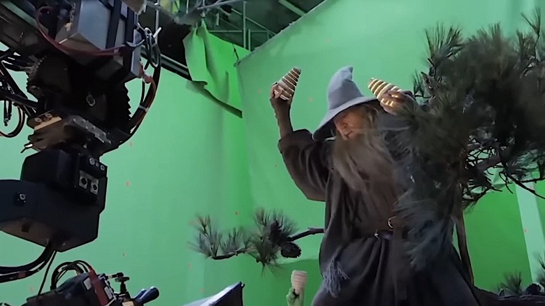 Ian McKellen lifts fake pinecones up to throw while in tree with greenscreen and cameras surrounding him