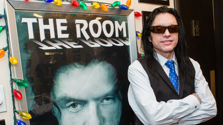 Wiseau posing with "The Room" poster