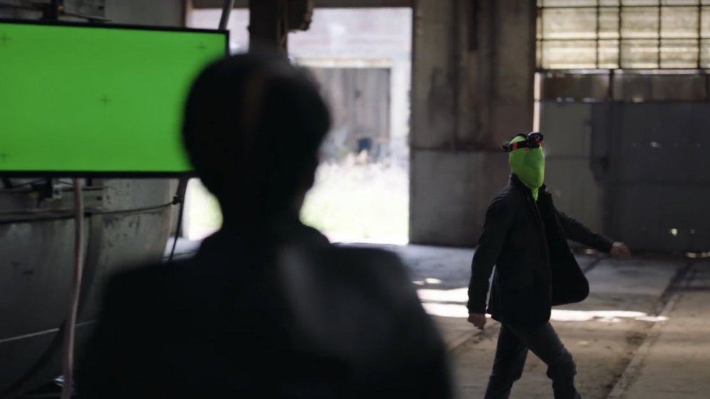 A man wearing a green mask walks toward a woman