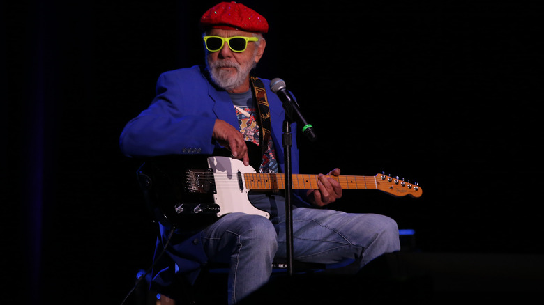 Tommy Chong with yellow sunglasses, a red hat, and guitar