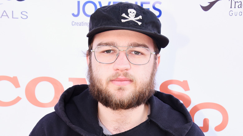 A bearded and bespectacled Angus T. Jones wearing a hat at the Combsgiving Festival in 2016