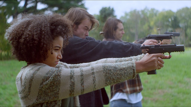 A woman and two men stand in a line firing guns in a field