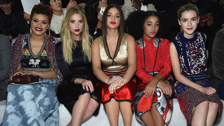 A group of young women sit in a row at a fashion show