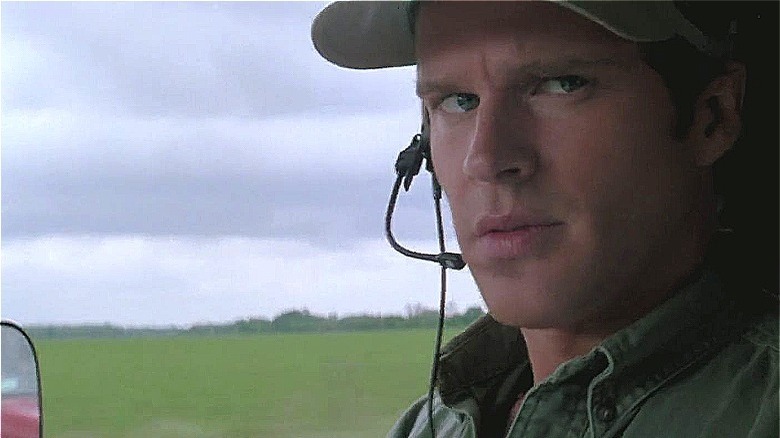 cary elwes in car window, ball cap and ear piece