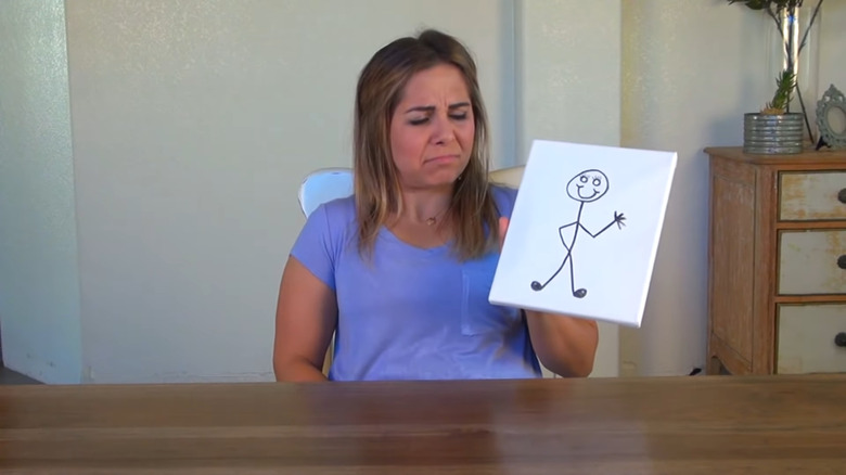 A woman holds a drawing of a stick figure