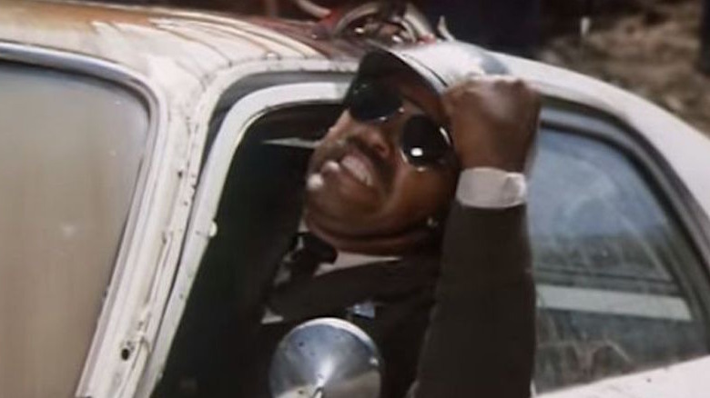 Don Pedro Colley, in sunglasses, grimaces and shakes a fist