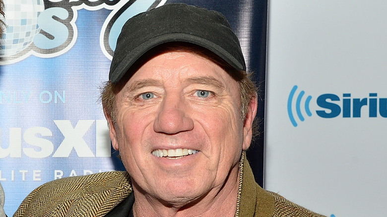 Tom Wopat smiles and wears a hat